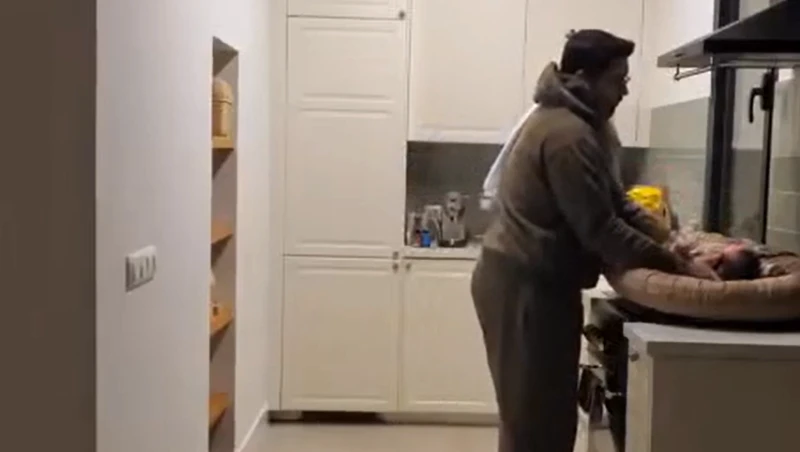 Vader verschoont een baby op een fornuis onder een afzuigkap in een keuken.