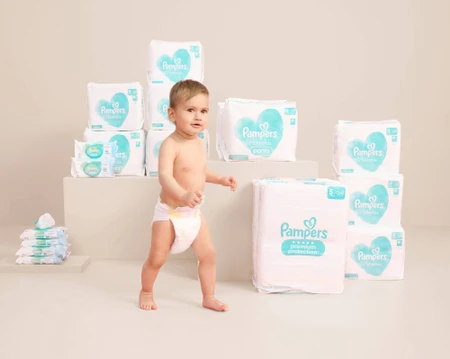 Peuter in luiers omringd door stapels luiers op een neutrale achtergrond.