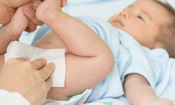 Baby ligt op een bedje en de billen worden schoongemaakt met een babydoekje