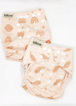 Twee AliRose herbruikbare pocket luiers in zacht perzik met narwal en hemel prints en verstelbare drukknopen